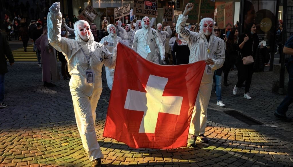 Protesters wearing mask depicting syringes hold a Swiss flag during a rally against the current measures to tackle the spread of the coronavirus, Covid-19 health pass and vaccination, in Lausanne on October 16, 2021. - On 28 November 2021, Swiss will vote on challenging the law underpinning many of the governments coronavirus measures. The countrys vaccination rate is lower than that of many other European nations. (Photo by Fabrice COFFRINI / AFP) (Photo by FABRICE COFFRINI/AFP via Getty Images)