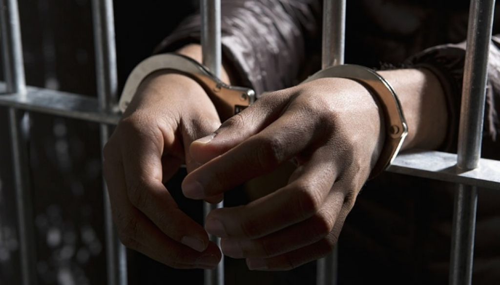 Seorang tahanan di balik jeruji besi dengan tangan diborgol - Stok Foto via Getty Image