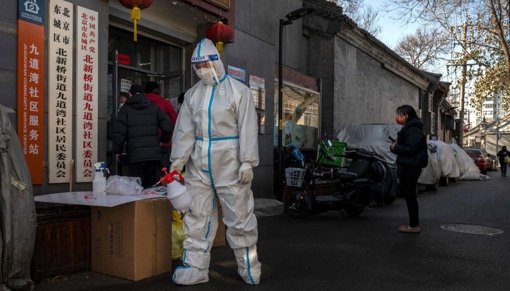 Seorang pekerja pengendalian epidemi mengenakan APD saat membersihkan area di luar kantor kesehatan setempat yang membagikan obat-obatan dan tes antigen cepat di lingkungan tradisional pada 8 Desember 2022 di Beijing. (Foto oleh Kevin Frayer/Getty Images)