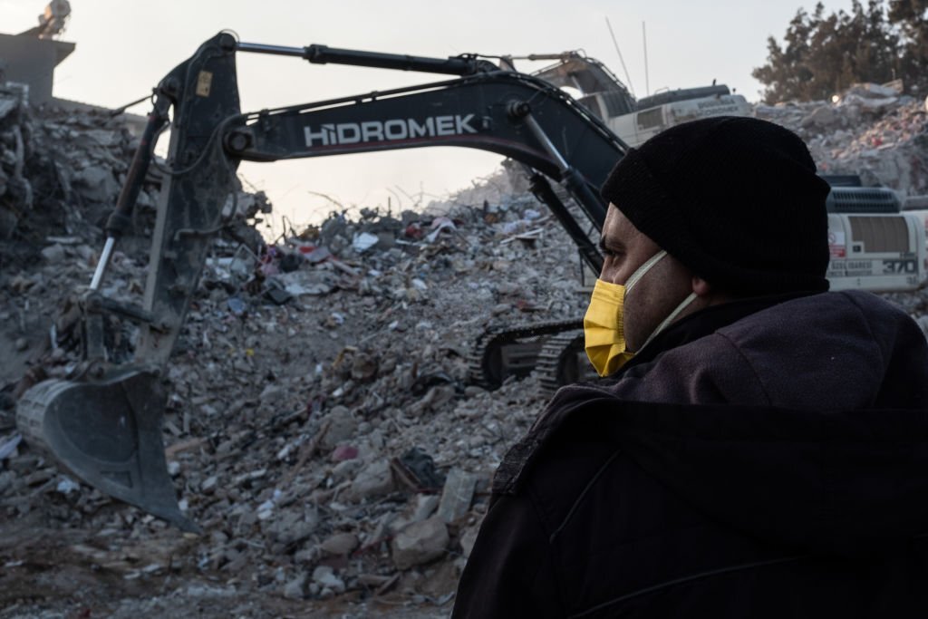 Seorang pria menyaksikan ekskavator bekerja di lokasi bangunan yang runtuh untuk mengangkat puing-puing pada 16 Februari 2023, di Hatay, Turki. (Foto oleh Burak Kara/Getty Images)