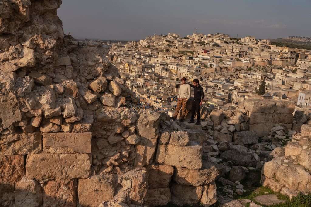 Dua pemuda Suriah berdiri di kasel Harim, kasel militer tua itu bertanggal 959 M agak rusak oleh gempa bumi, menikmati matahari terbenam dan pemandangan kota yang terletak di perbatasan Turki, pada 24 Februari 2023 di utara Idlib, Suriah. (Foto oleh Abdulmonam EASSA/Getty Images)