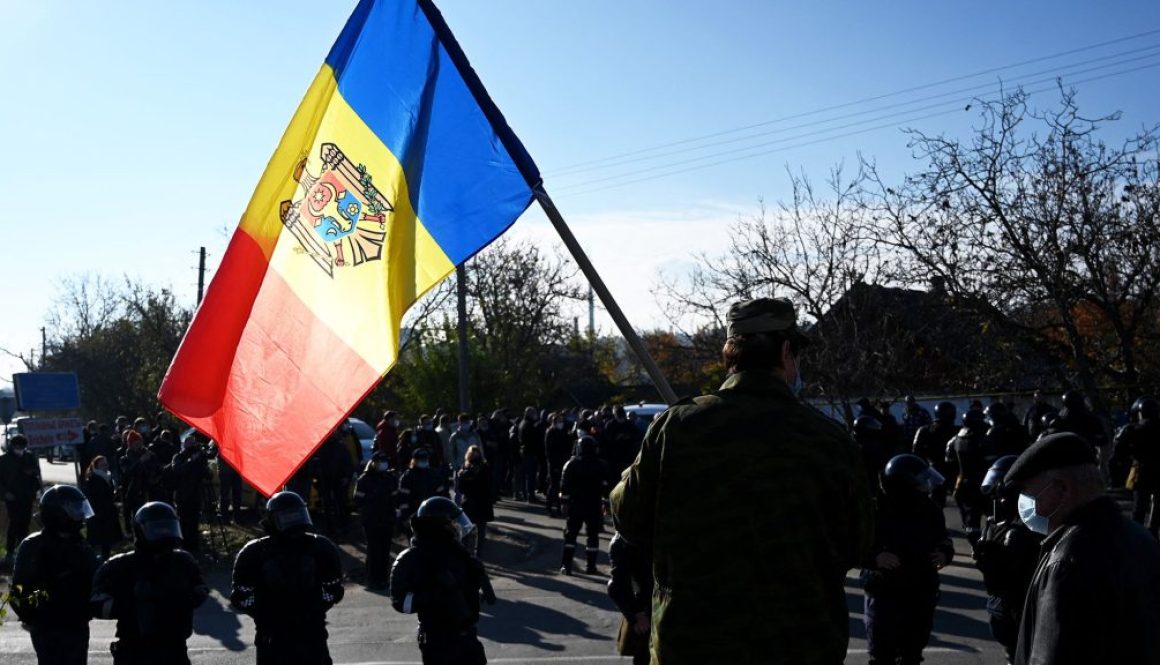 A man holds Moldovan national flag as special police officers patrol a street near a polling station during the second round of Moldova's presidential election in the town of Varnita at Moldova - Transnistrian border on November 15, 2020, amid the ongoing Covid-19 pandemic.