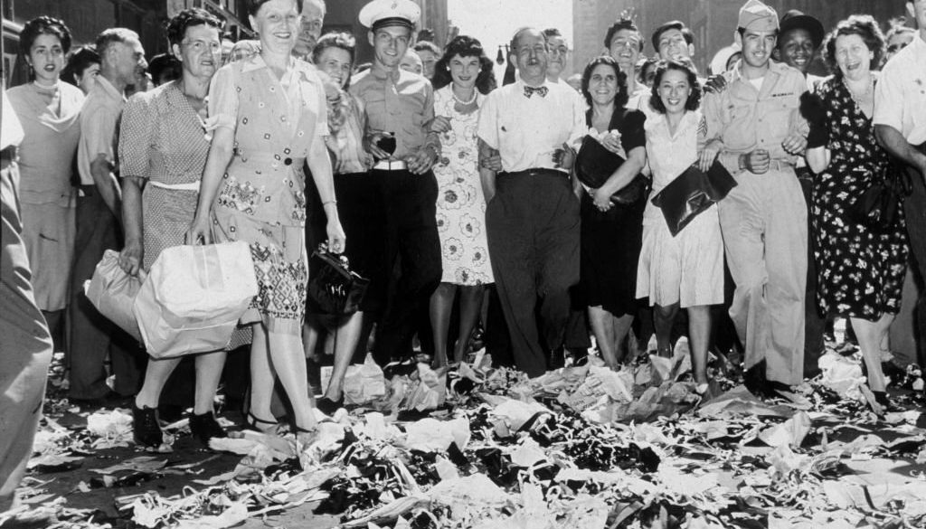 American servicemen and civilians smile as they celebrate news of the Japanese surrender and the end of World War II, Times Square, New York City. Piles of ticker tape lie in the street. Japanese forces formally surrendered to the Allies in a ceremony aboard the U.S.S. Missouri on September 2, 1945. (Photo by New York Times Co./Getty Images)