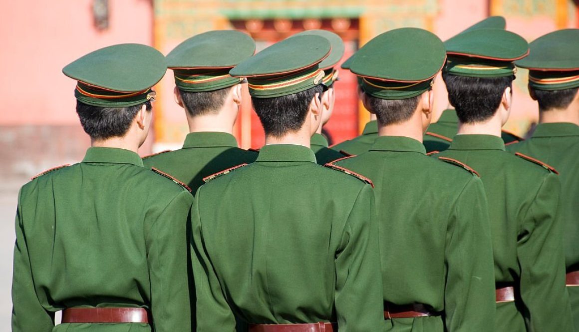 Unrecognizable group of soldiers standing in line and seen from behind. Wearing uniforms including caps. The soldiers belong to the Chinese armed forces.